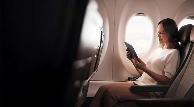 Female sitting in A220 economy looking at iPad